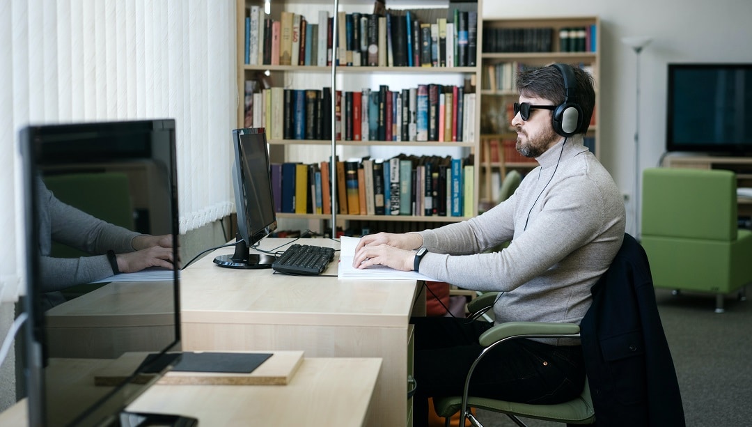 Een meneer leest op de achtergrond braille en op de voorgrond staat een computerscherm uit