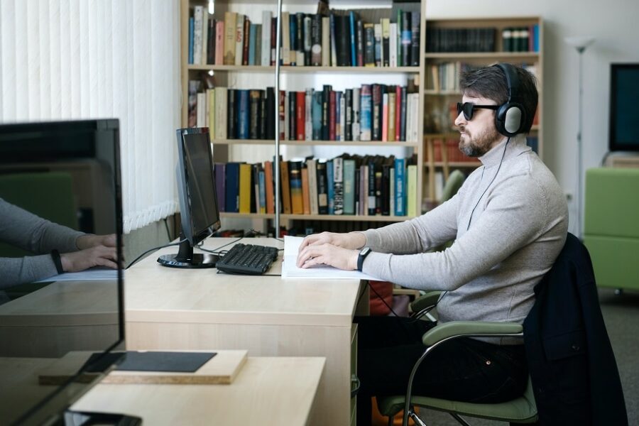 Een meneer leest op de achtergrond braille en op de voorgrond staat een computerscherm uit