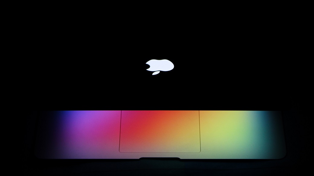 In het pikkedonker schijnt regenboogkleurig licht uit een half dichtgeklapte laptop van Apple