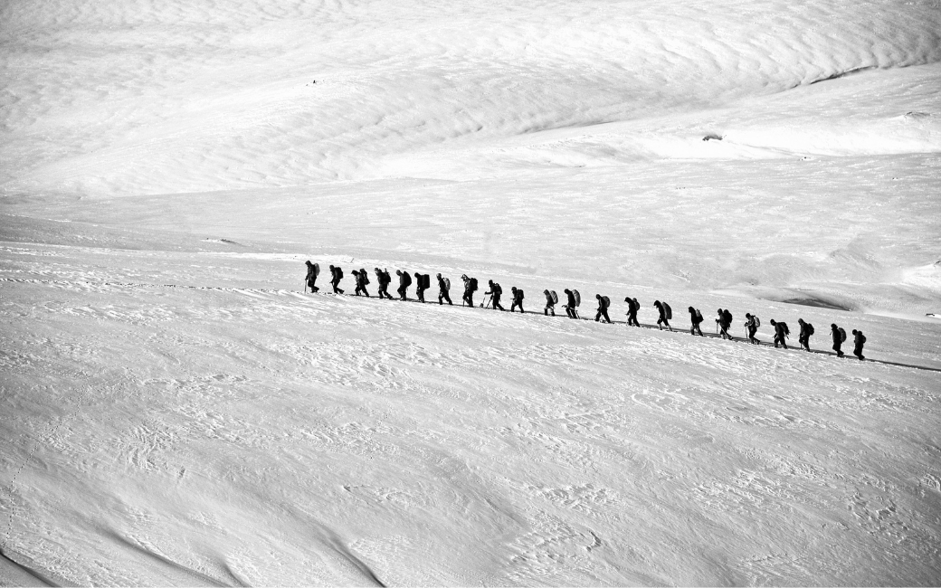 Een groep bergbeklimmers loopt tegen een besneeuwde helling op omhoog.