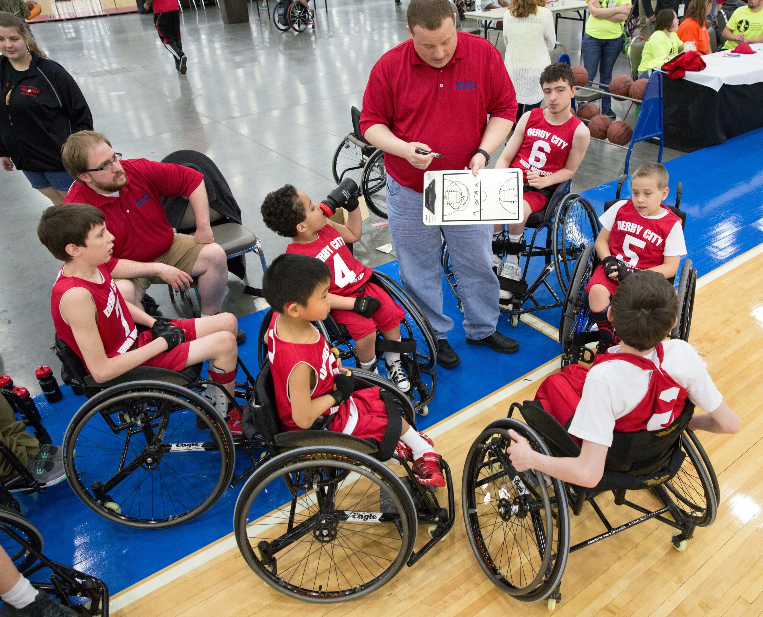 Een groep kinderen krijgt uitleg tijdens een wedstrijd rolstoel-basketbal