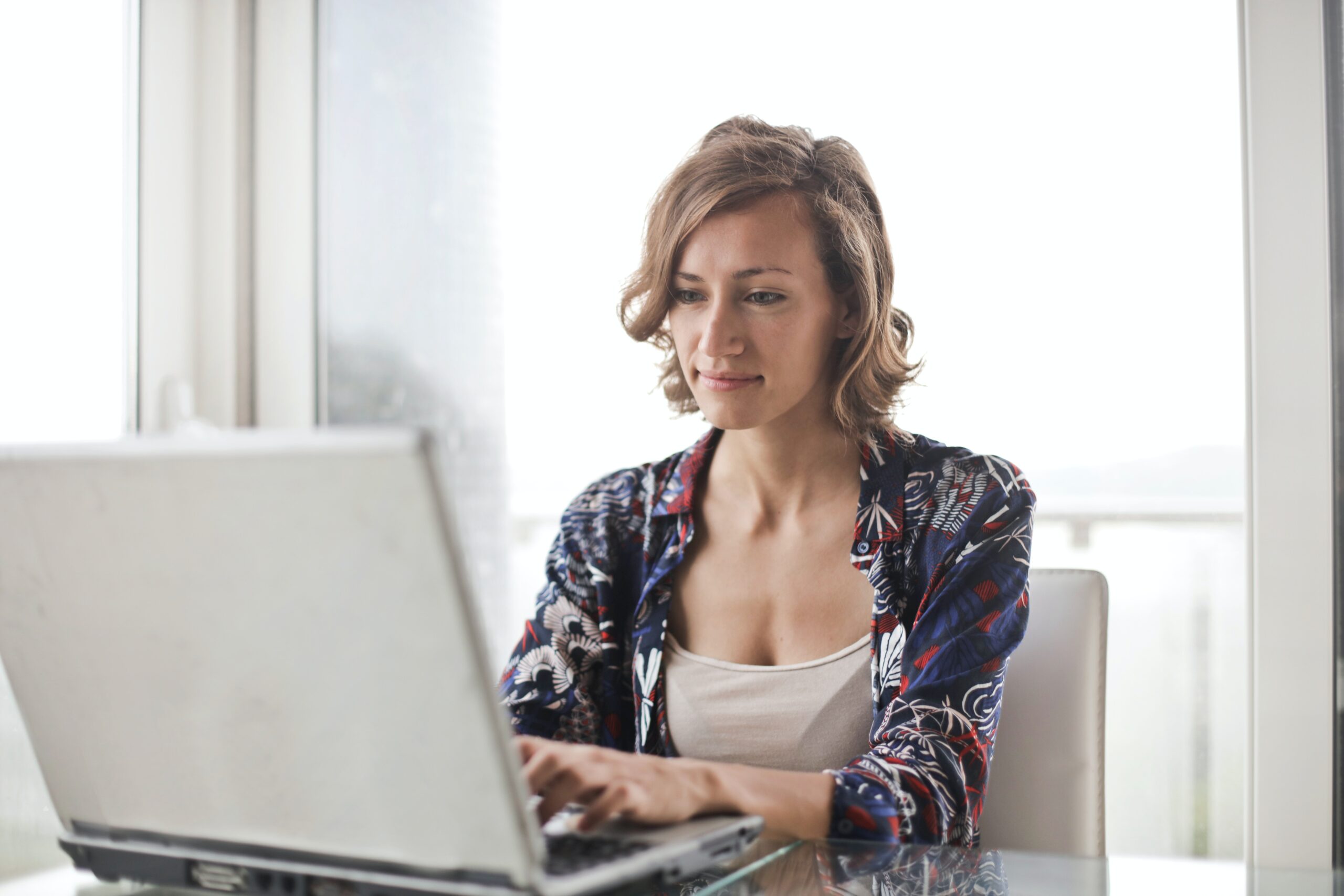 Een blonde vrouw zit tevreden te werken aan haar bureau met laptop