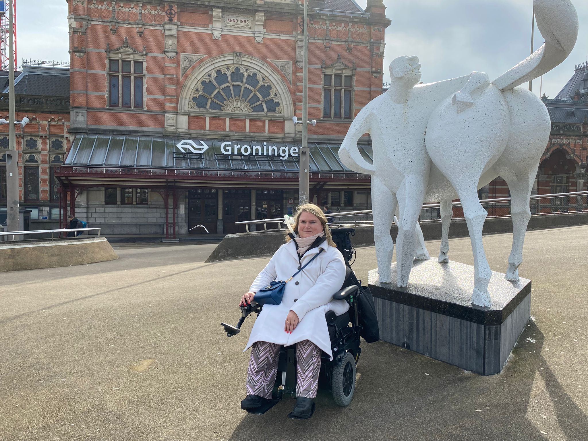 Judith voor het station in Groningen bij een wit standbeeld met een man en een paard