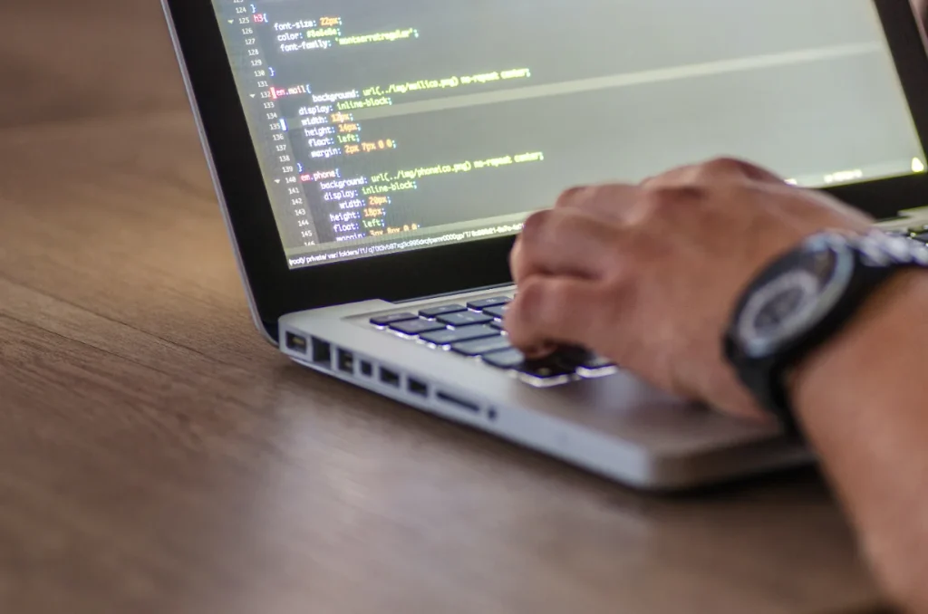 Een hand typt HTML-code op een laptop in