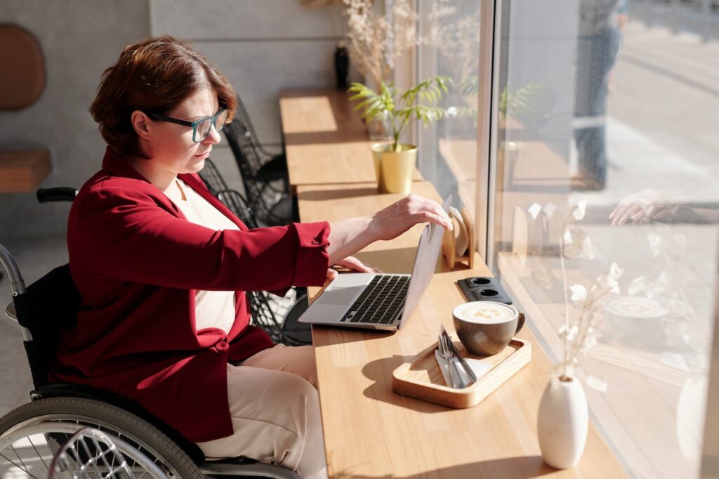 Vrouw in rolstoel kijkt naar laptop in een cafe