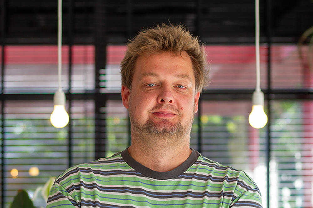 David kijkt met een glimlach in de camera. Op de achtergrond zie je het kantoor van digitaal toegankelijk