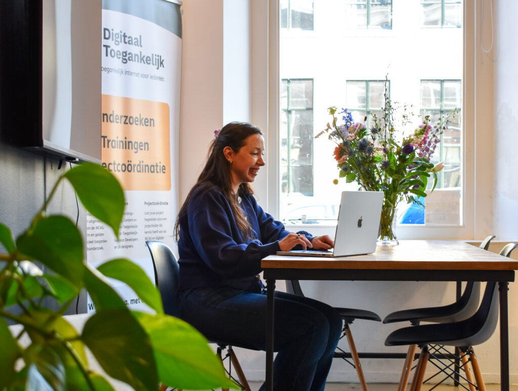 Talissa zit aan een tafel te werken naast een groot raam in het kantoor van Digitaal Toegankelijk