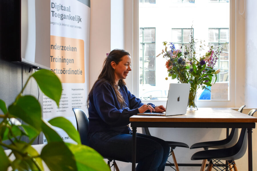 Talissa zit aan een tafel te werken naast een groot raam in het kantoor van Digitaal Toegankelijk