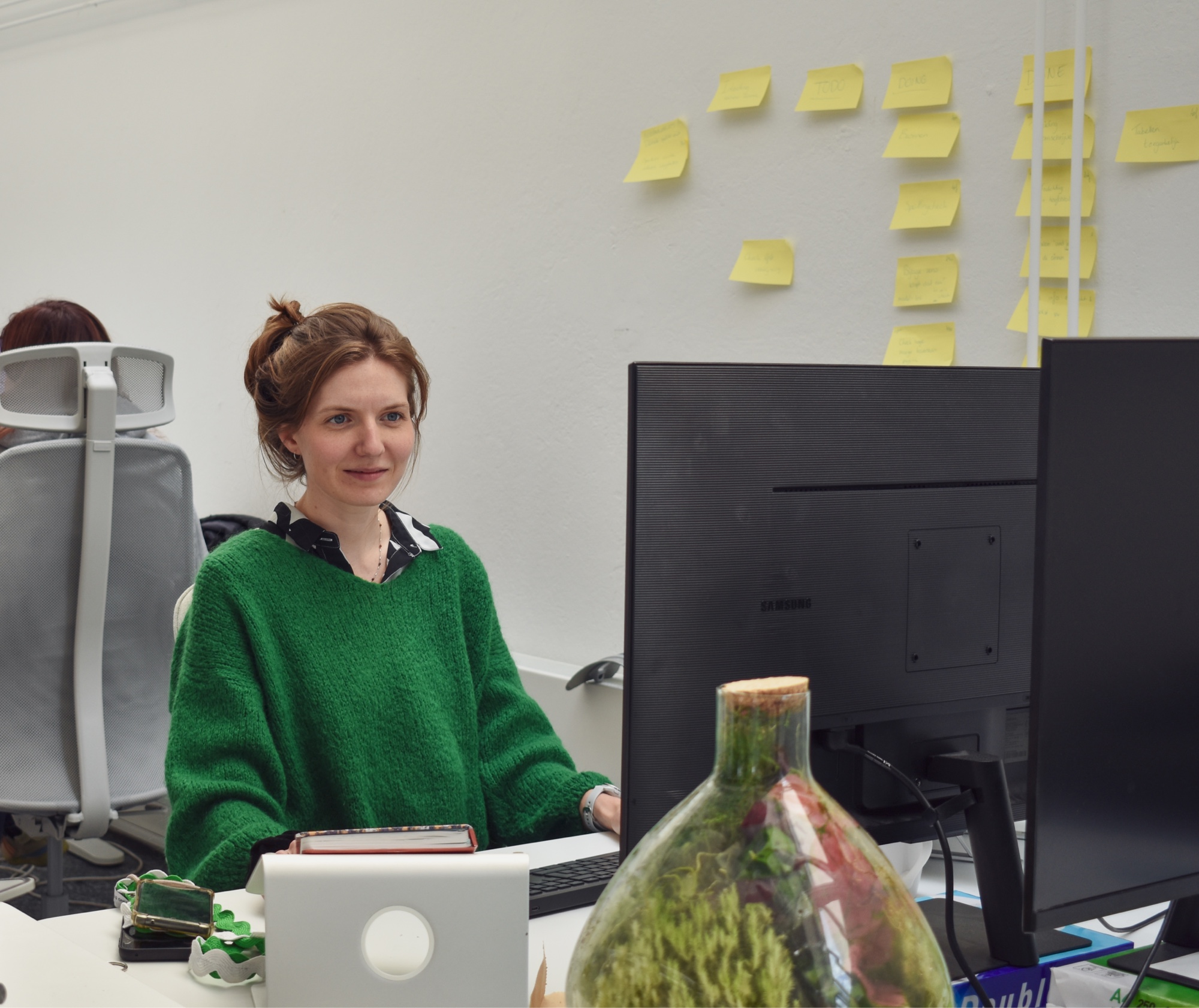 Aafke kijkt naar haar scherm in het kantoor van digitaal toegankelijk. Op de achtergrond zie je een rijtje gele post-its op de muur.