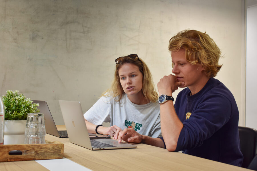 Steffi en Menno zitten in een overlegruimte in het kantoor van Digitaal Toegankelijk. Ze kijken samen naar een laptop.
