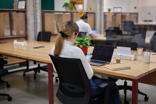 vrouw zit op telefoon en aan bureau staat haar laptop open