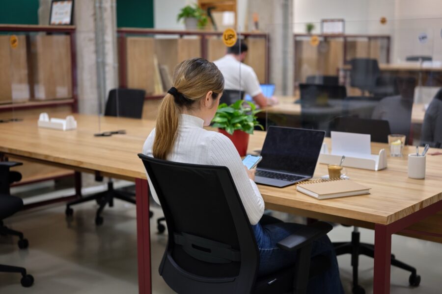 vrouw zit op telefoon en aan bureau staat haar laptop open