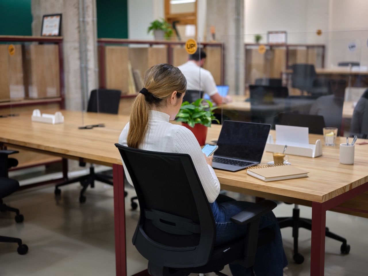 vrouw zit op telefoon en aan bureau staat haar laptop open